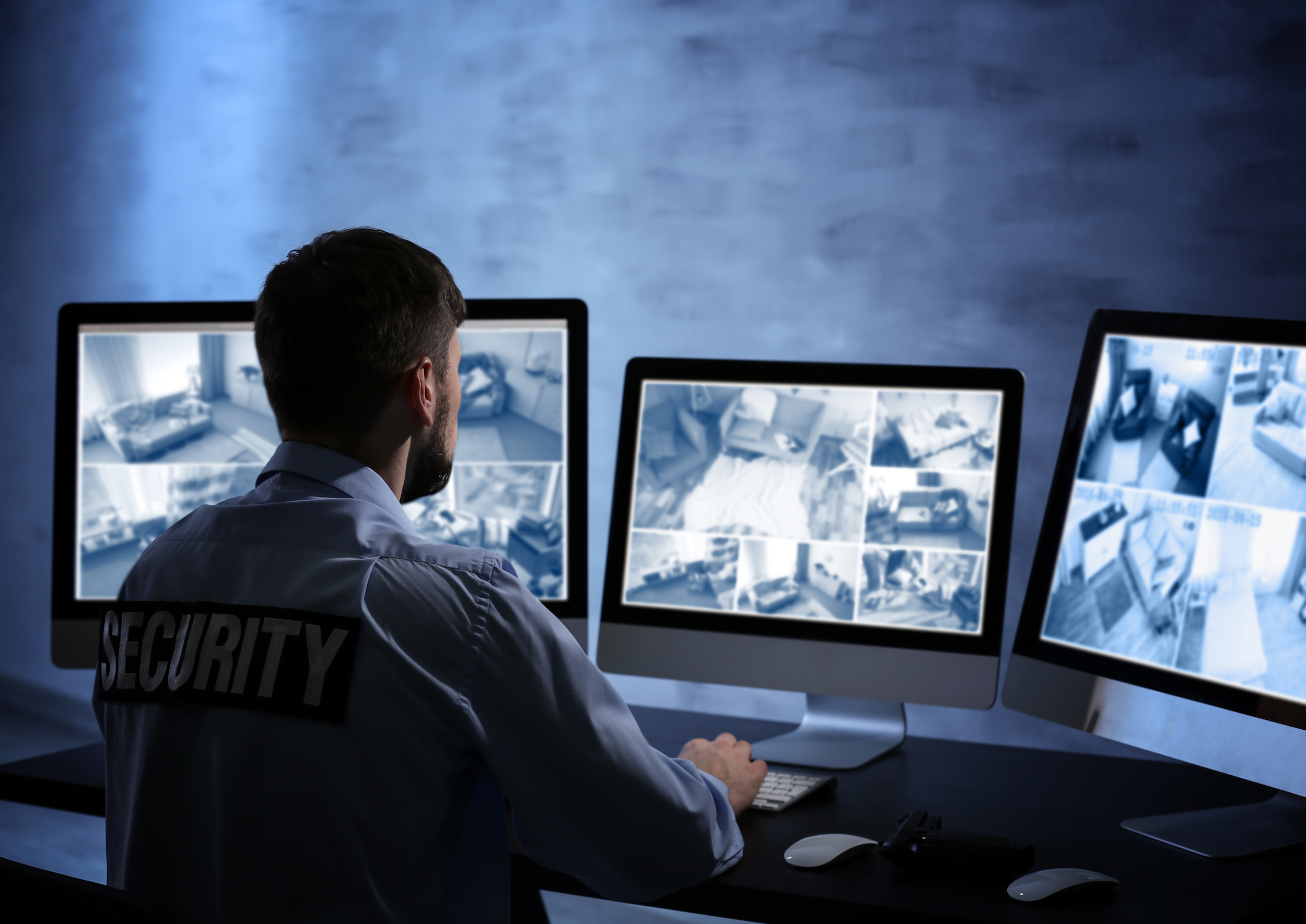 A security guard sitting at his desk looking at three monitors.